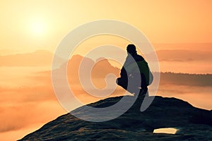 Rear view of male hiker sitting on the rocky peak while enjoying a colorful daybreak above mounrains valley