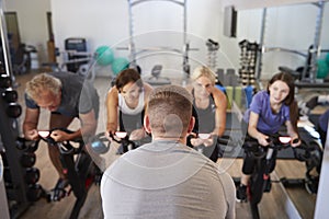Rear View Of Male Trainer Taking Spin Class In Gym photo