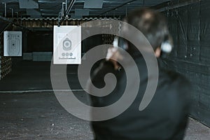 rear view of man aiming gun at target in shooting range