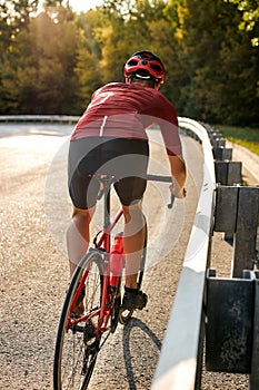 rear view on man with athletic body shape in protective helmet riding bicycle