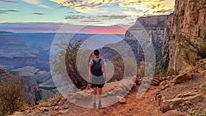 Rear view of man with backpack hiking along Bright Angel trail with panoramic aerial overlook of South Rim of Grand Canyon