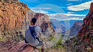 Rear view of man with backpack hiking along Bright Angel trail with panoramic aerial overlook of South Rim of Grand Canyon