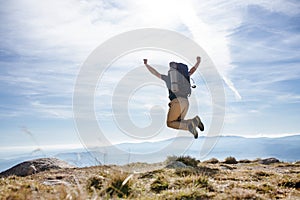 Rear view of man with backpack hiking in mountains in summer, jumping.