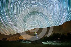 rear view of man climbed on a rock looking at star trails at night