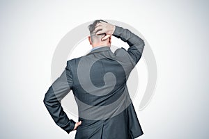 Rear view, a man in a dark jacket thinks and scratches his head with his hand, on light background.