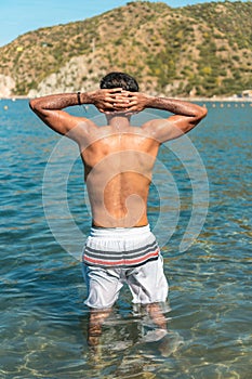 Rear view of man with his hands on his head on the beach. Man on the beach with his hands on his head, back view of the boy,