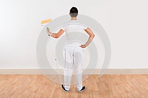 Rear View Of Man Holding Paint Roller Against White Wall
