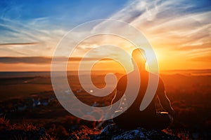 Rear view of the man meditating yoga in lotus pose on the rock at sunset.