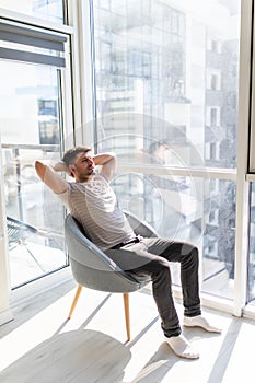 Rear view of man relaxing on chair at home near window