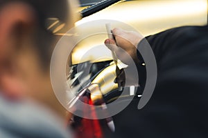 Rear view of man removing dents from body of car using bright lamp. Professional car repair and detailing in a garage