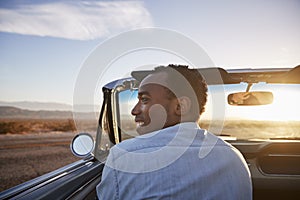 Rear View Of Man On Road Trip Driving Classic Convertible Car Towards Sunset