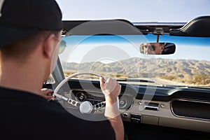 Rear View Of Man On Road Trip Driving Classic Convertible Car Towards Sunset