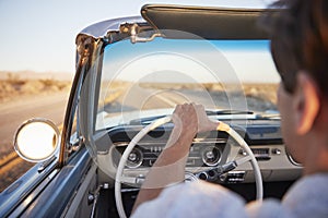 Rear View Of Man On Road Trip Driving Classic Convertible Car Towards Sunset