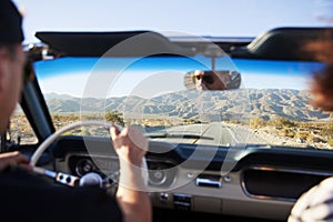 Rear View Of Man On Road Trip Driving Classic Convertible Car Towards Sunset