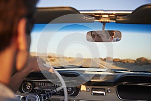 Rear View Of Man On Road Trip Driving Classic Convertible Car Towards Sunset