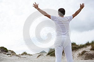 Rear view of man standing with arms outstretched on beach