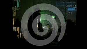 Rear view of a man standing in front of glass board in dim lighted room, leaning on the table and thinking. Stock