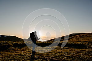 Rear view man standing on the hill field with hiking backpack and sticks