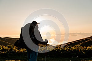 Rear view man standing on the hill with hiking backpack and sticks