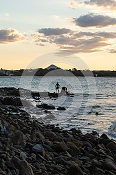 Rear View of Man Standing on Rocks in front of the Ocean Watching the Sunset. Traveler Concept