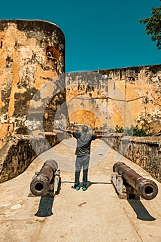 Rear view of man standing between two ancient canons at the entrance of Fort Jesus in Mombasa, Kenya