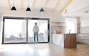 Rear view of man standing in unfurnished house, moving in new home concept.