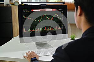 Rear view of man trader investor analyzing digital exchange stock market charts graphs on computer screen
