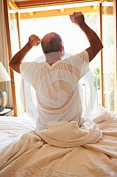 Rear View Of Man Waking Up In Bed In Morning