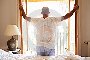 Rear View Of Man Waking Up In Bed In Morning