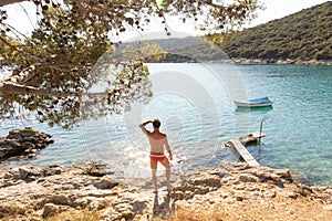 Rear view of man wearing red speedos tanning and realaxing on wild cove of Adriatic sea on a beach in shade of pine tree