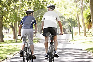 Rear View Of Mature Couple Cycling Through Park