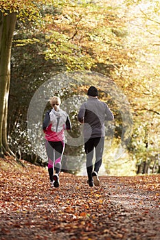 Rear View Of Mature Couple Running Through Autumn Woodland