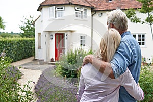 Rear View Of Mature Couple Standing In Garden Look At Dream Home In Countryside