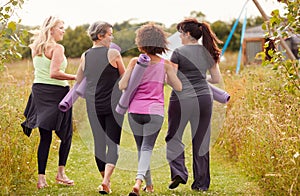 Rear View Of Mature Female Friends On Outdoor Yoga Retreat Walking Along Path Through Campsite