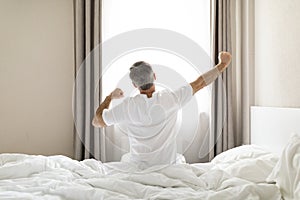 Rear view of mature man in pajamas stretching in bed