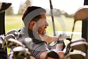 Rear View Of Mature Man Playing Golf Driving Buggy Along Course Viewed Through Golf Clubs