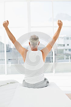 Rear view of mature man stretching arms in bed