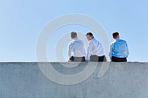 Rear view of mature thoughtful businessmen sitting on office rooftop