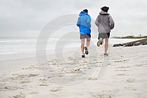 Rear view, men and running on beach, sand and fitness for wellness and gym wear in cold coast. Male athletes, jog and