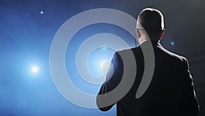 Rear view of men speaking through a microphone in dark conference hall. Person says about marketing and management for