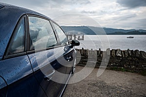 Rear view of modern luxury dark blue car parked above the Loch Lomond in Luss with a romantic view