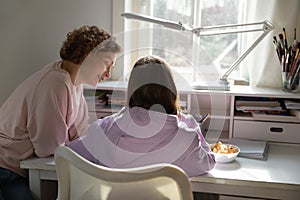 Rear view of mom helping teen daughter with homework