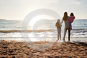 Rear View Of Mother With Daughters Looking Out To Sea Silhouetted Against Sun