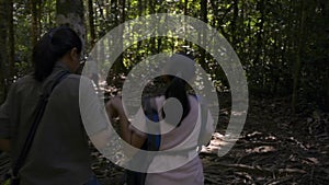 Rear view of mother and her daughter are walking hand in hand together on hiking trail along the stream.