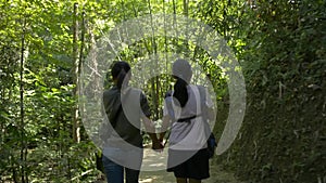 Rear view of mother and her daughter are walking hand in hand together on hiking trail along the stream.