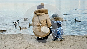 Rear view of mother with little boy feeding ducks on cold winter day at park