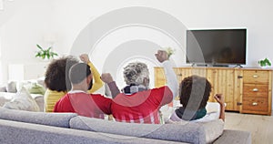 Rear view of Multi-generation family cheering while watching sports on TV at home