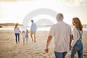 Rear view of Multi generation family holding hands and walking along the beach together. Caucasian family with two