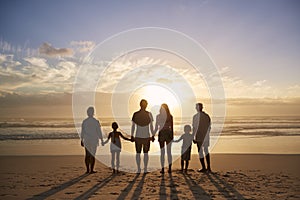 Rear View Of Multi Generation Family Silhouetted On Beach