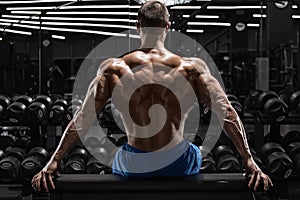 Rear view muscular man showing back muscles at the gym. Strong male naked torso, workout